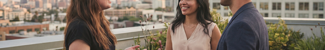 Three people engaged in a conversation on a rooftop with city skyline in the background